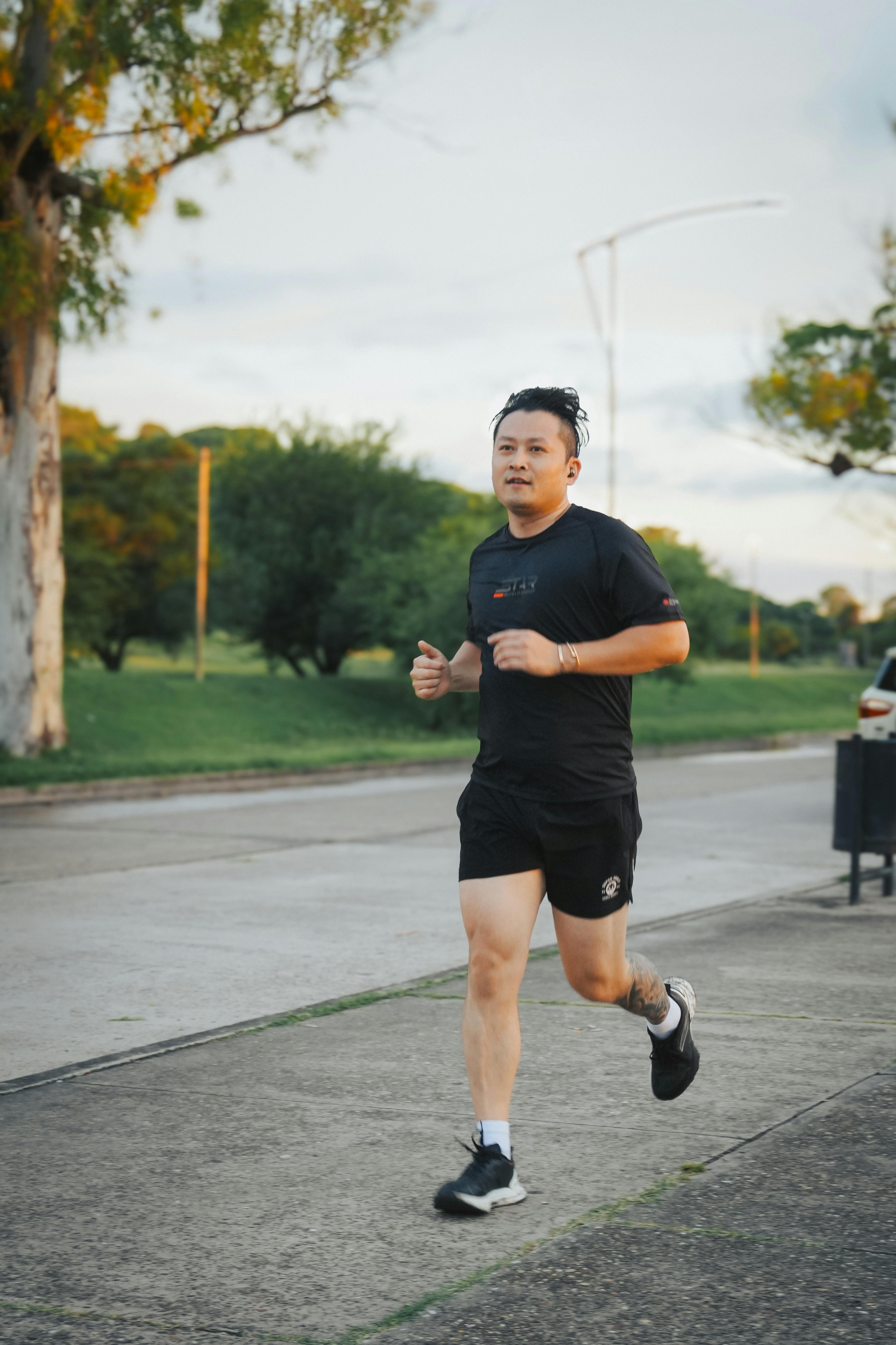 A man jogs along a suburban street in athletic wear during the day, surrounded by greenery.