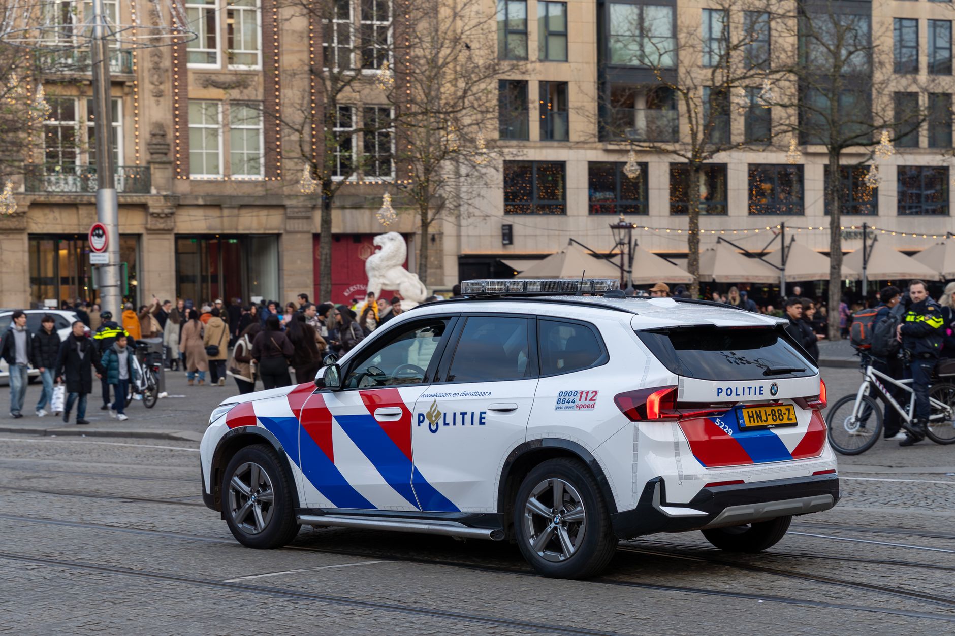 Dutch police car patrols busy street in Amsterdam with people and bicycles in the background.
