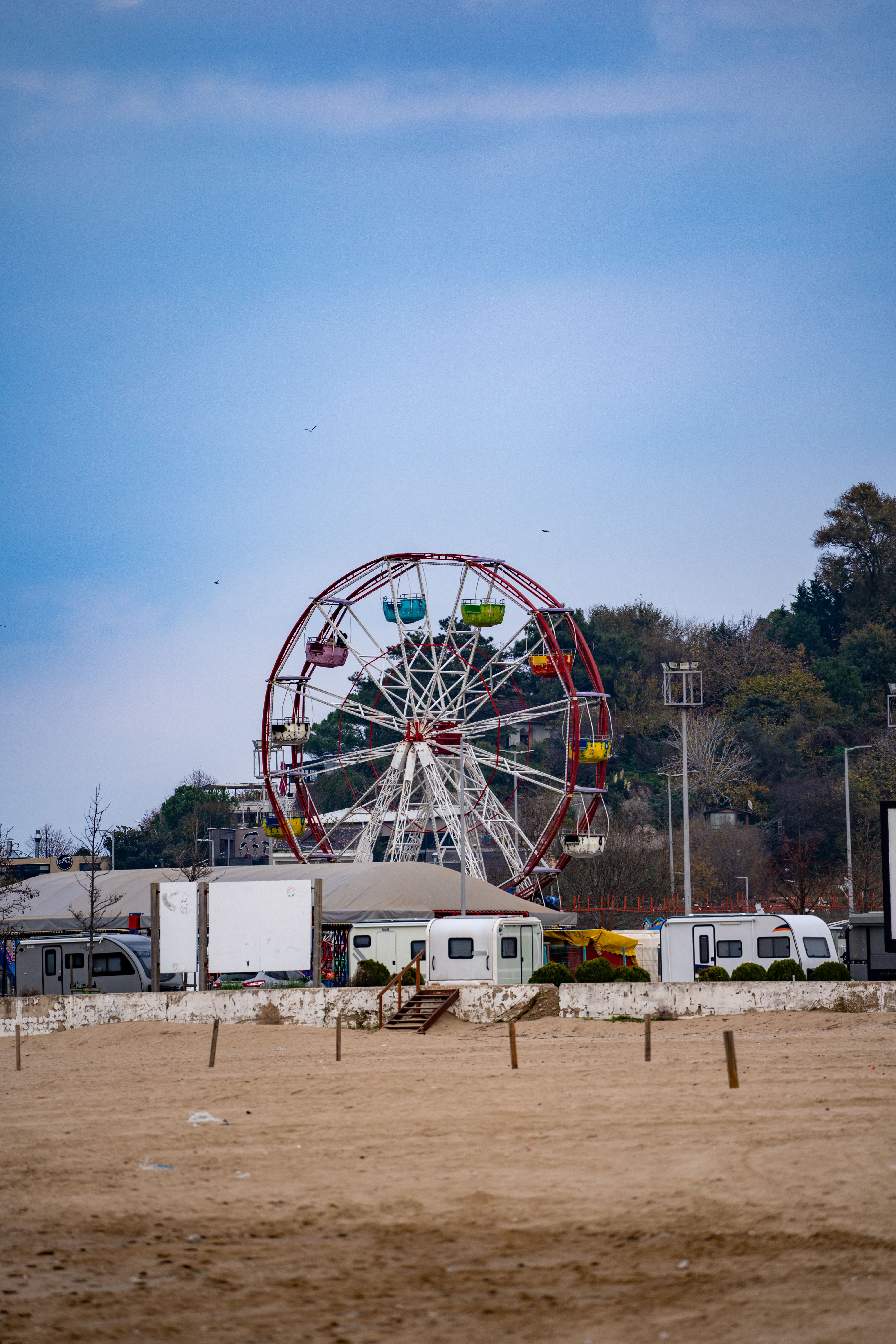 Fotomural Noria colorida en un parque de atracciones frente a la playa en un día nublado.