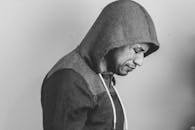 一张在室内拍摄的黑白肖像，画面上是一位穿着连帽衫、神情深思的男人