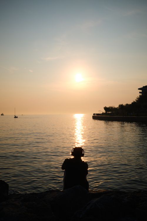 Free A tranquil scene of a person in headphones enjoying sunset by the sea. Stock Photo