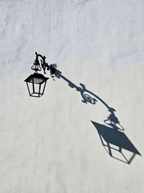 Free Artistic shadow of a vintage street lamp on a textured white wall. Stock Photo