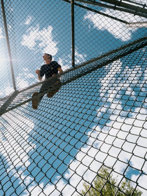 Free Man climbing a chain-link fence with blue sky and clouds background in Monsey, NY. Stock Photo