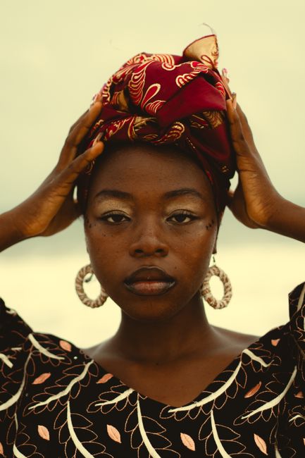 Striking portrait of a woman wearing a vibrant headwrap and earrings, set against a neutral background.