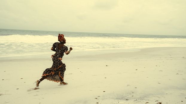 An African woman in a colorful dress joyfully runs along a tranquil beach