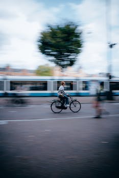 Blurred cyclist on Amsterdam street with tram in the background, capturing urban motion.