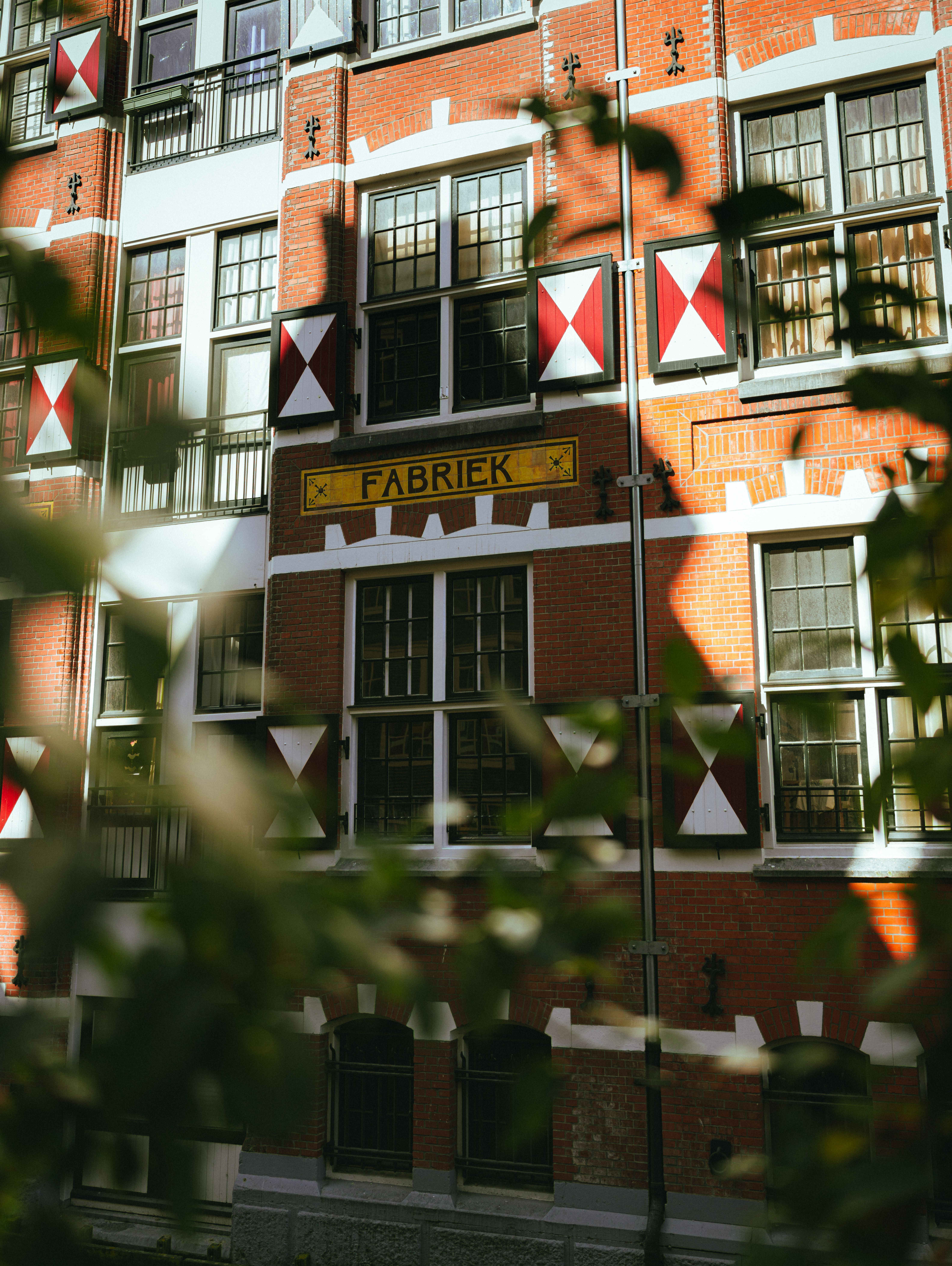 Red brick building in Amsterdam with 'Fabriek' sign and traditional shutters.