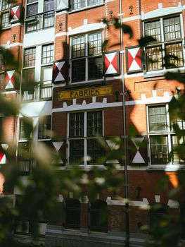 Red brick building in Amsterdam with 'Fabriek' sign and traditional shutters.