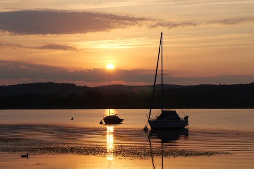 Serene sunset scene with boats reflecting on a calm lake surface.