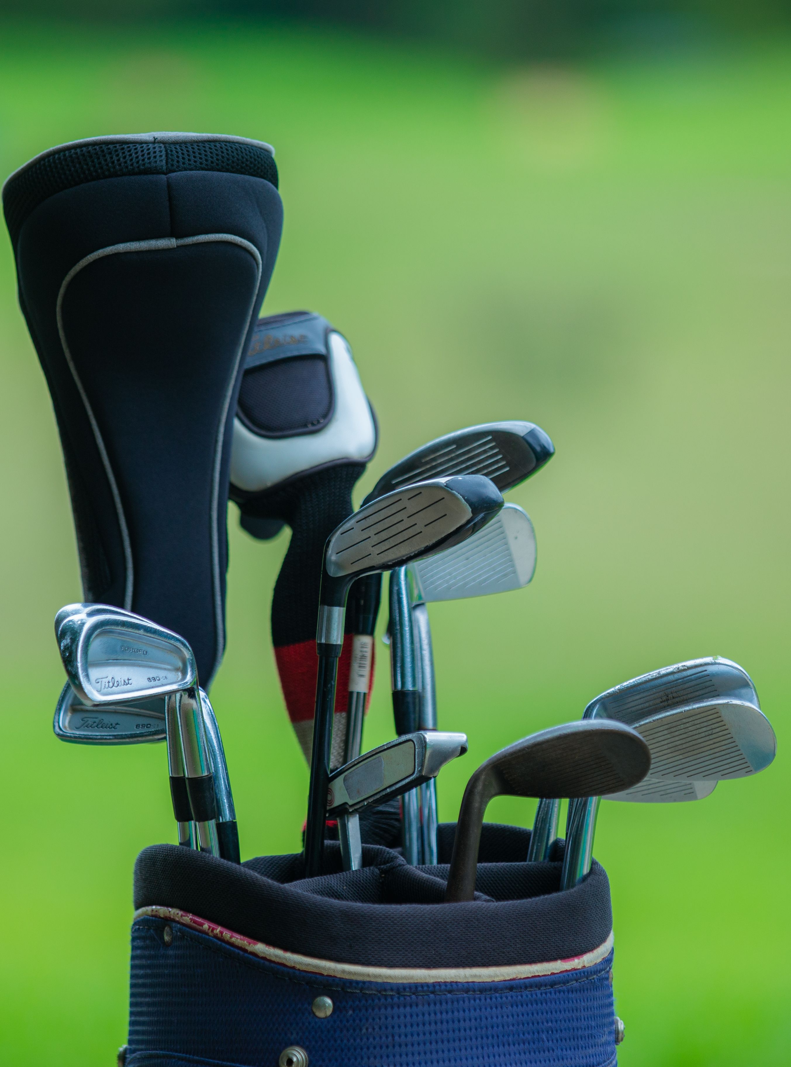 Close-up of golf clubs in a bag outdoors on a lush green background.
