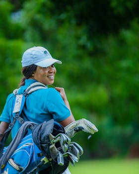 Smiling female golfer with clubs on a lush green course, under bright daylight.