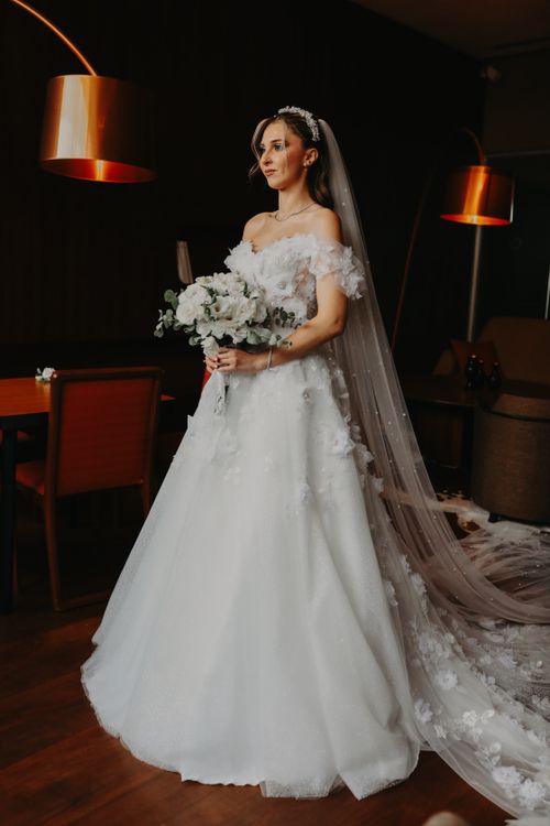 Free Beautiful bride in white wedding dress with floral bouquet, elegant and poised indoors. Stock Photo