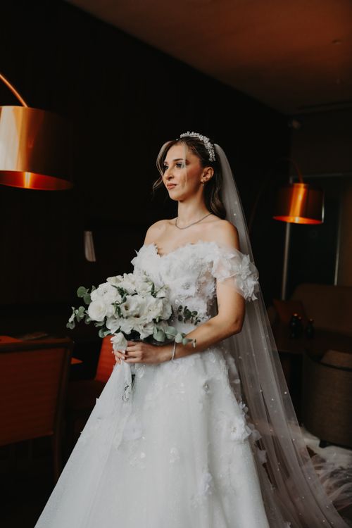 Free Elegant bride in white gown holding bouquet indoors. Warm lighting accentuates luxury. Stock Photo