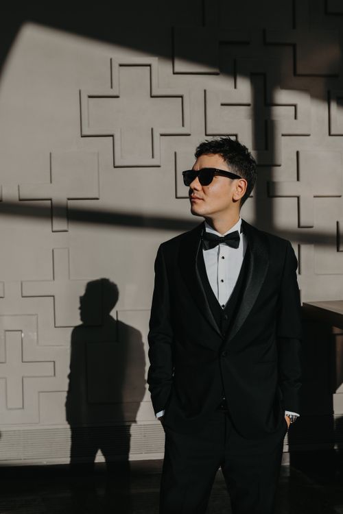 Free Elegant man in black tuxedo and sunglasses posing indoors with dramatic lighting. Stock Photo