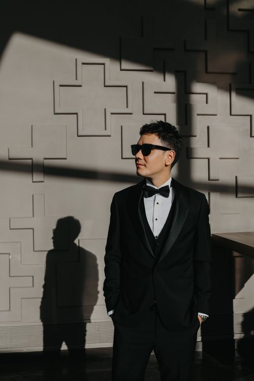 Free Man in tuxedo poses in sunlight, casting shadow on textured wall. Stock Photo