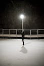 雪地里，一个孤独的人站在路灯下，灯光照亮四周，营造出一片宁静的冬日景象