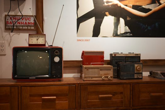 A collection of vintage TVs and radios on a wooden cabinet in a retro room.