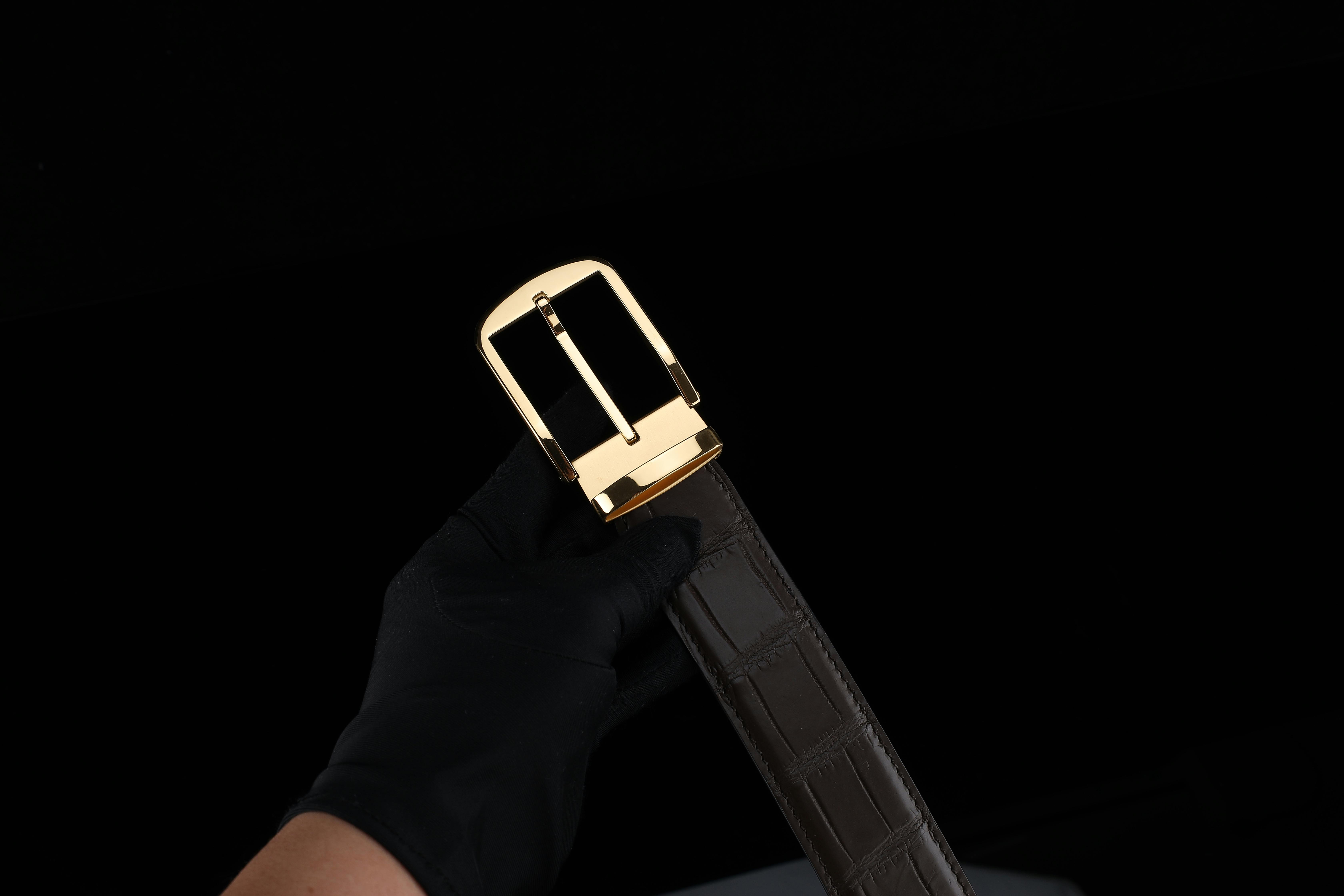 gratis Een close-up van een gehandschoende hand die een luxe leren riem met een gouden gesp vasthoudt. Stockfoto