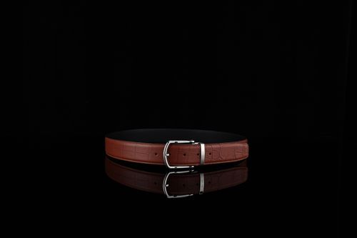 Free Stylish brown leather belt with silver buckle on shiny black background, ideal for fashion stock photos. Stock Photo