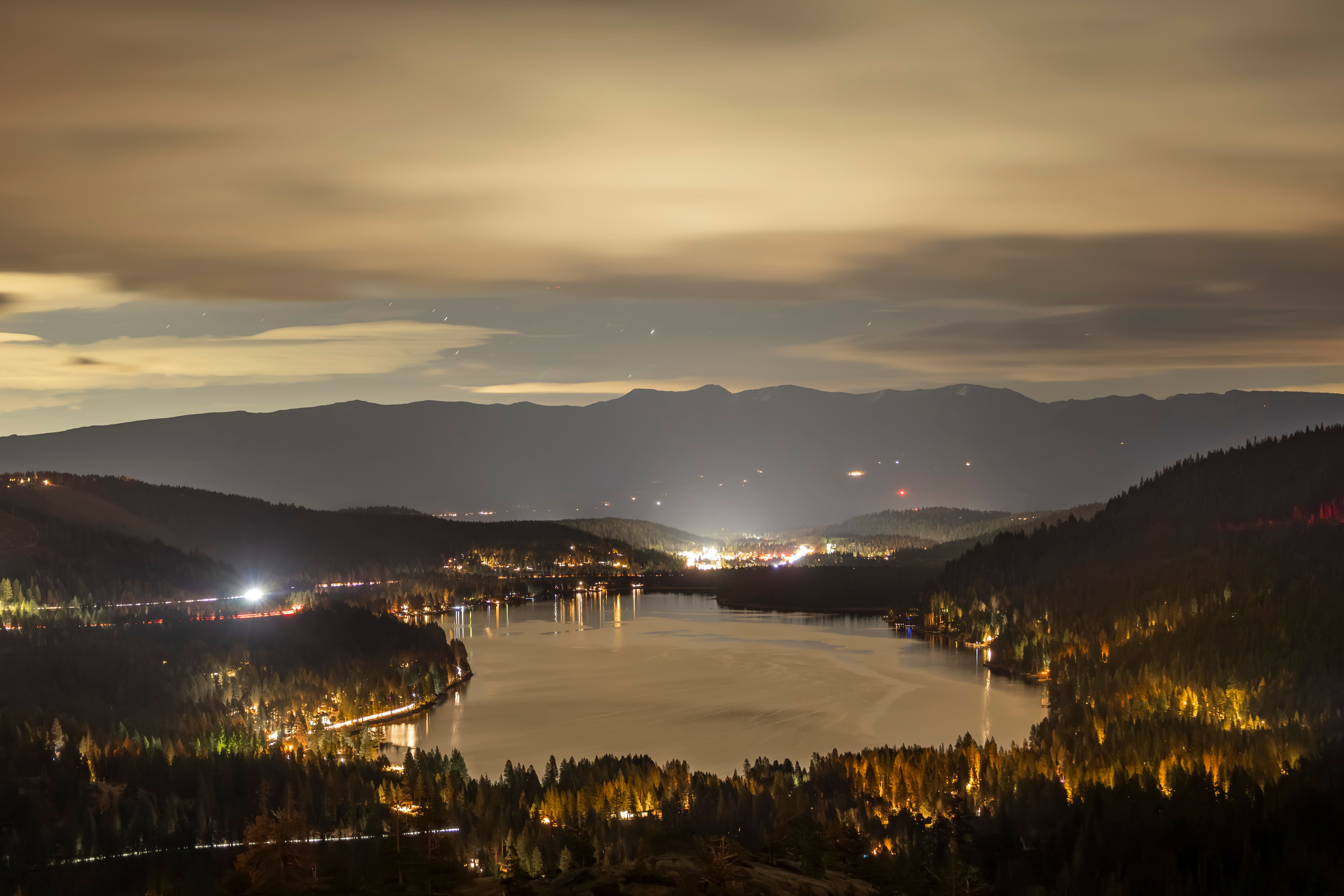 A breathtaking night view over Donner Lake with distant city lights under a cloudy sky.