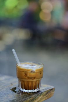 Chilled iced coffee with straw on rustic wooden table outdoors, blurred bokeh.
