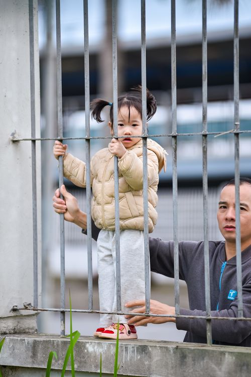 Free A young child with an adult outdoors, standing near metal bars, conveying everyday life. Stock Photo