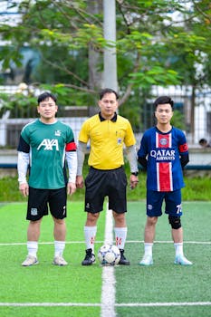 Three men pose at a soccer field in Vietnam, showcasing teamwork and sports spirit.