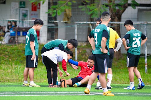 Teammates help an injured player during a soccer match on an outdoor field in Hà Nội, Việt Nam.