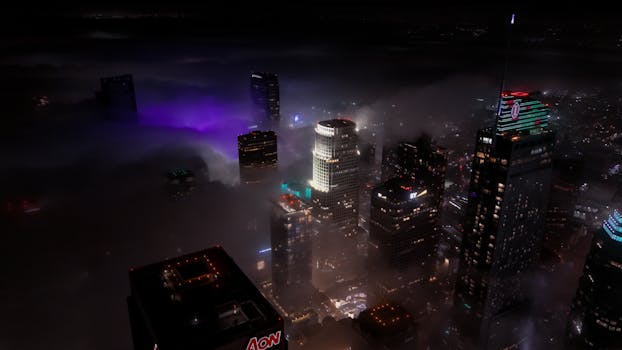 A stunning aerial view of skyscrapers enveloped in fog and city lights at night.