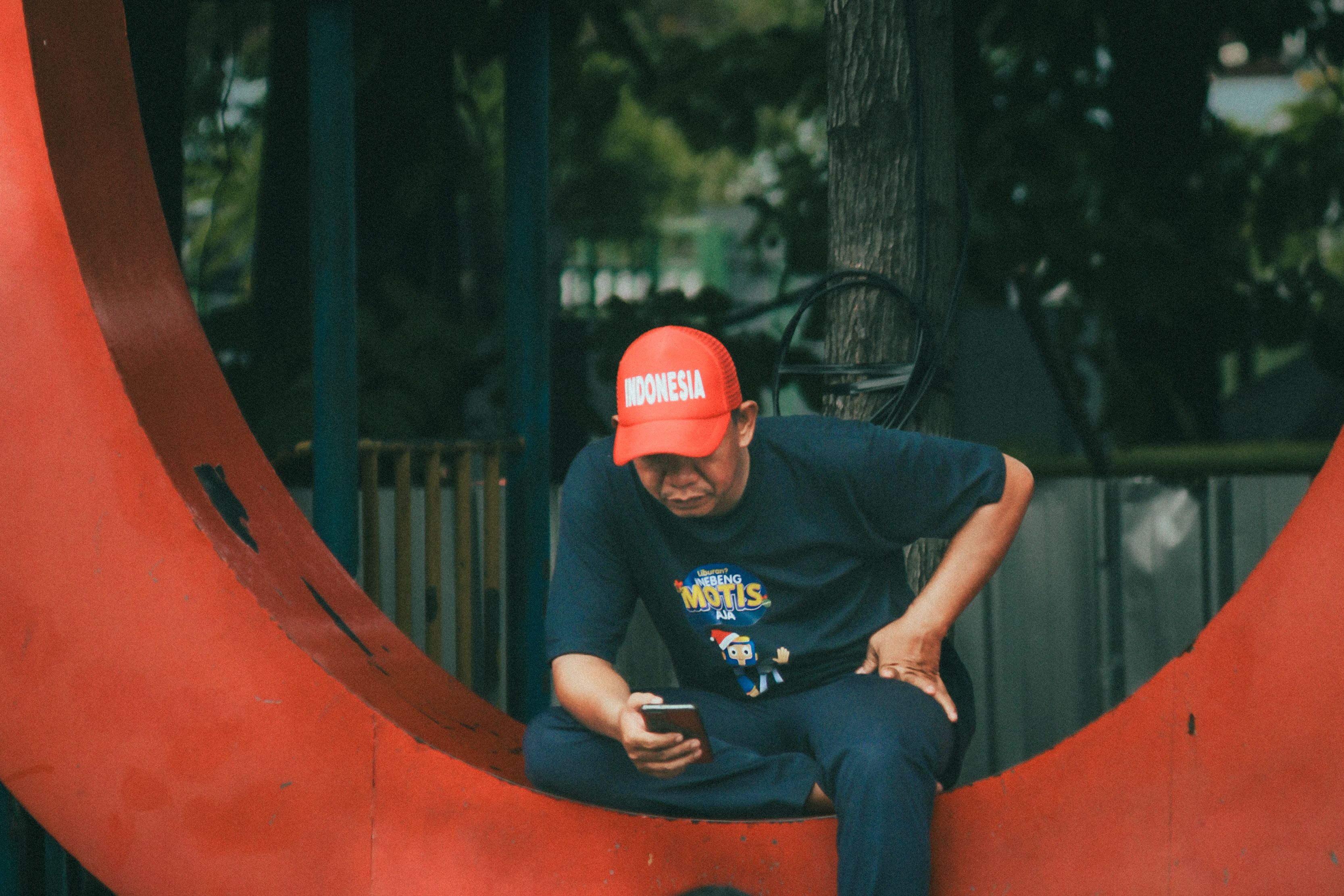 Man in Red Cap Using Smartphone Outdoors