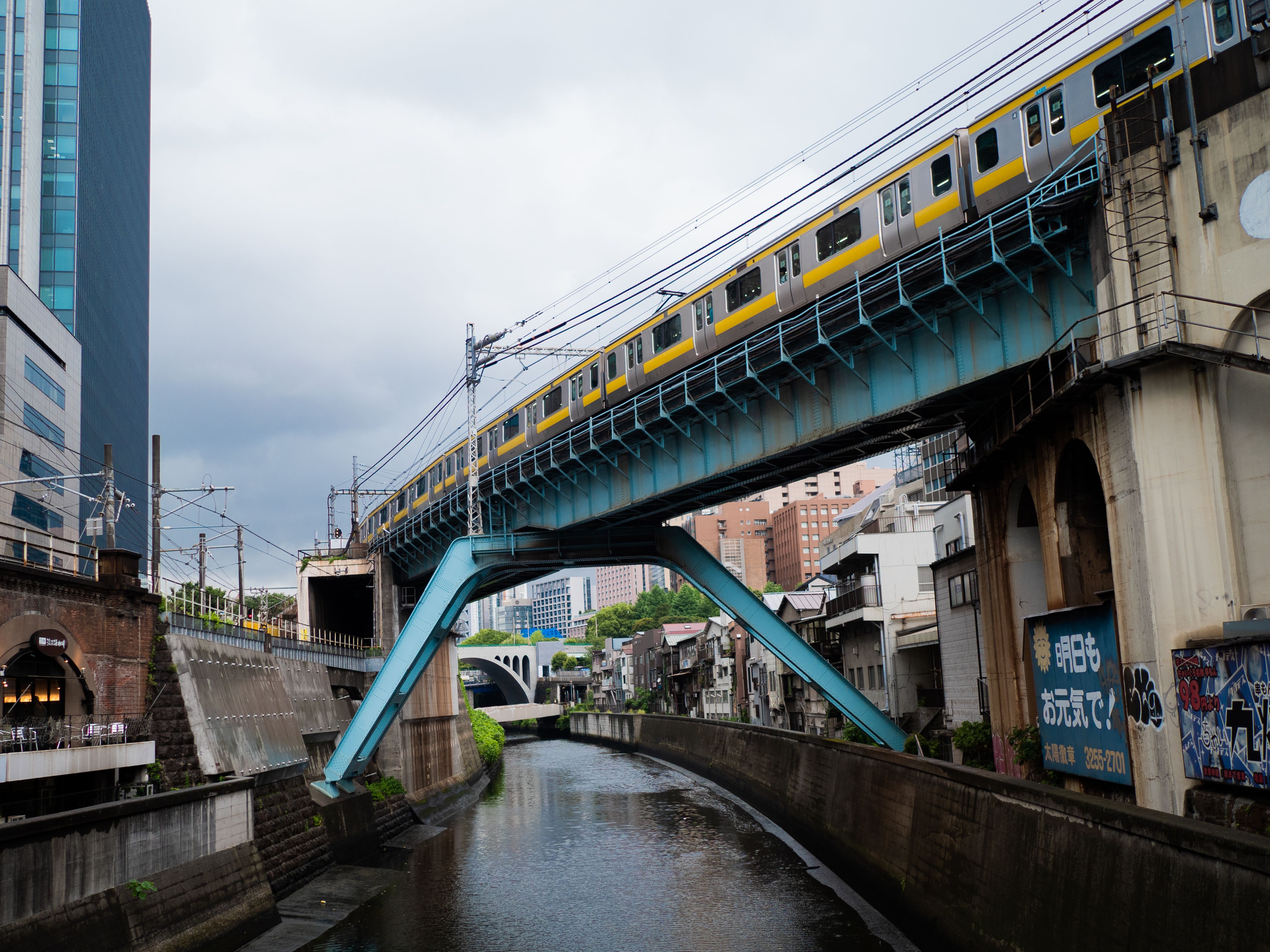 Yellow train traverses a bridge in dynamic Tokyo cityscape, showcasing urban architecture.