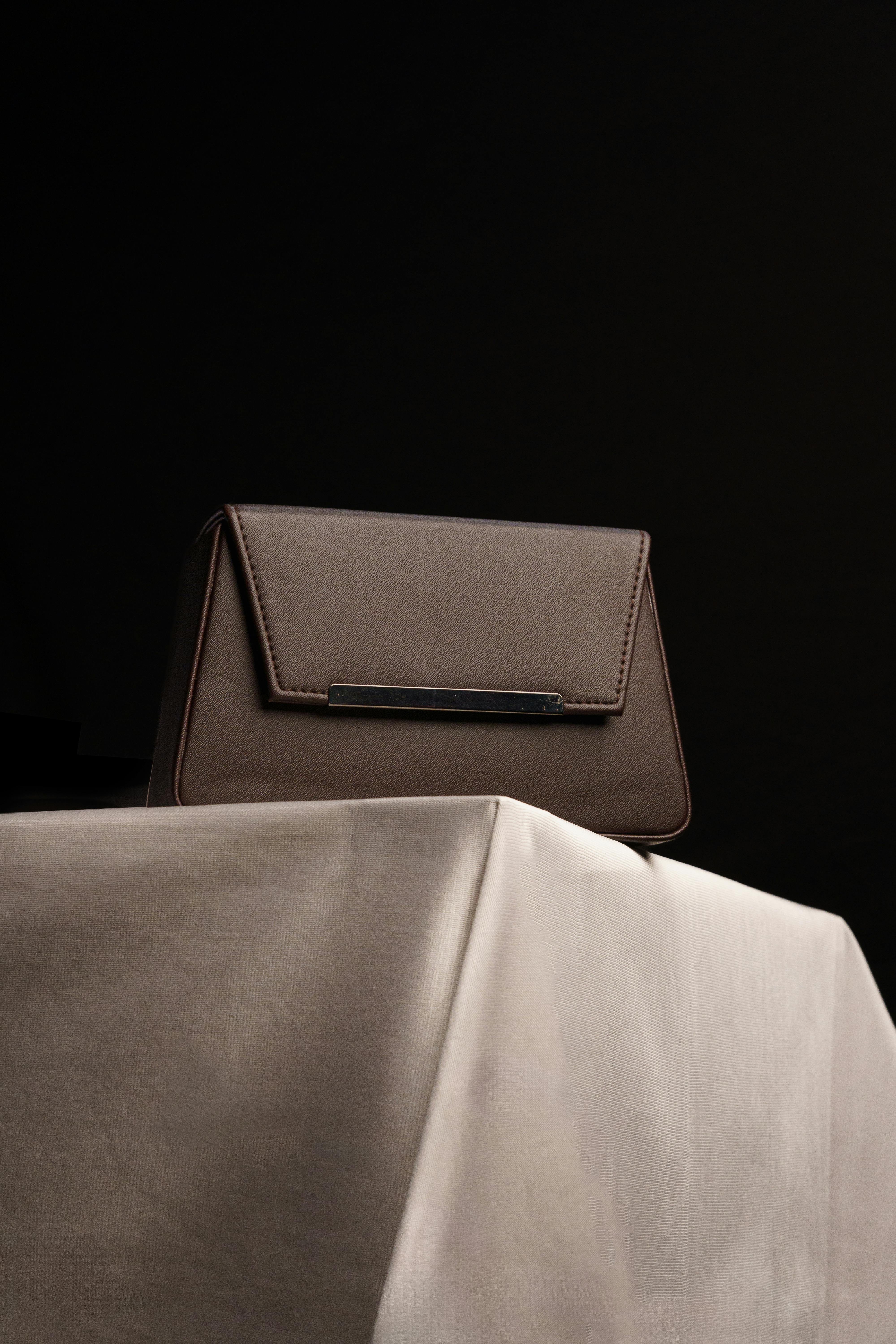 бесплатная Изящная коричневая кожаная сумочка элегантно выставлена на столе на темном фоне. Стоковое фото