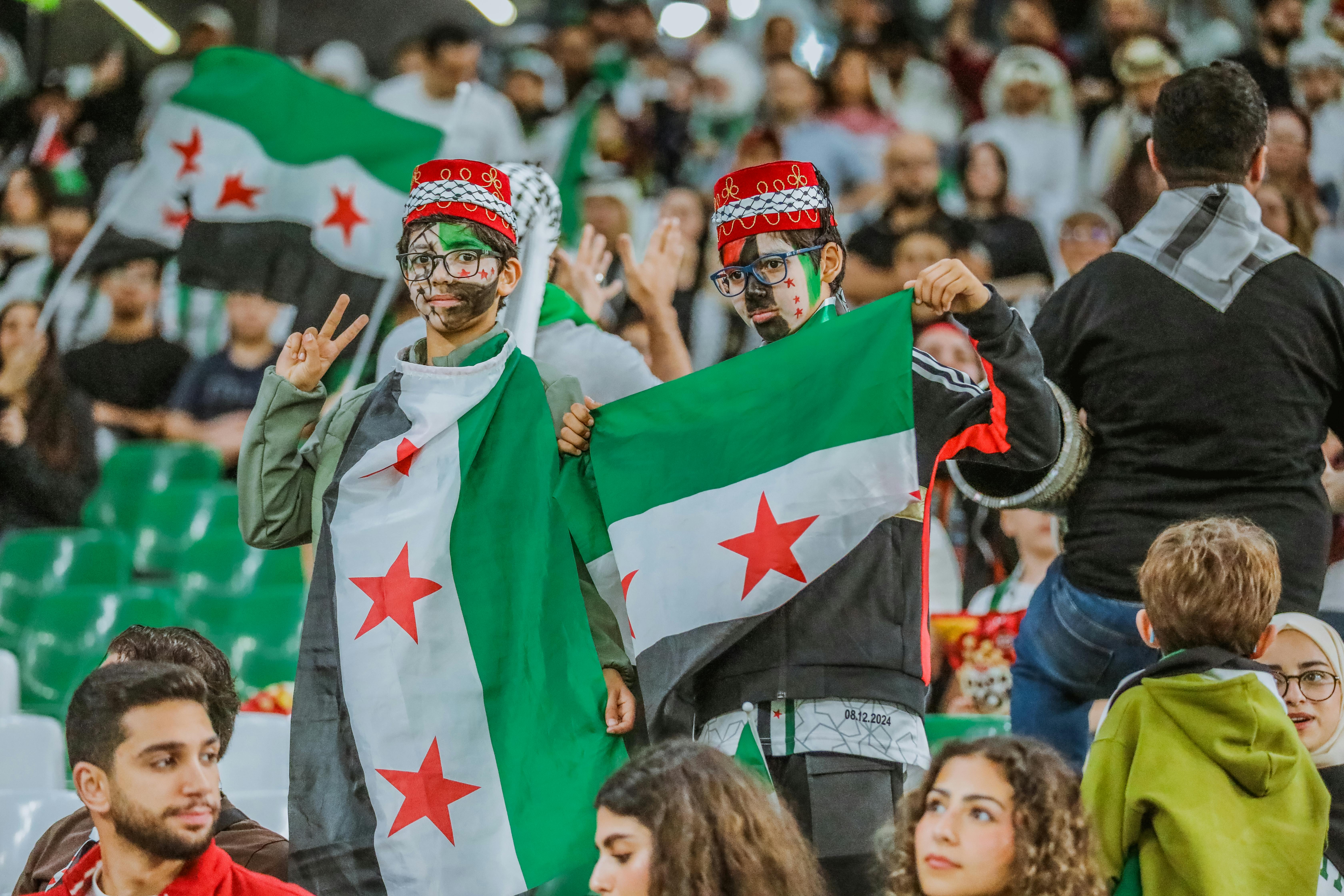 Supporters with Syrian flags at a sports event in Doha, capturing the vibrant and festive spirit.