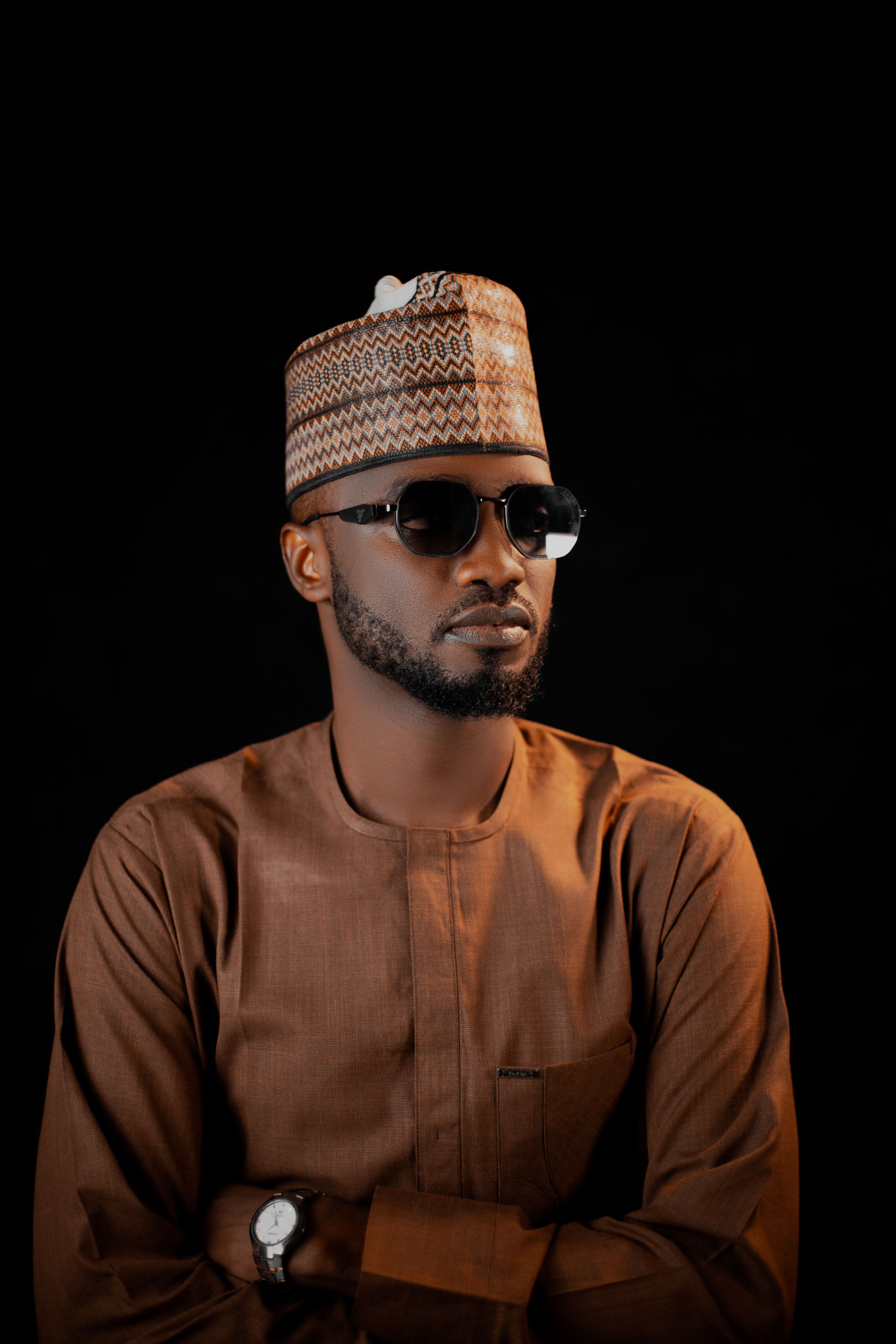 Confident man in traditional African clothing with sunglasses against dark background.