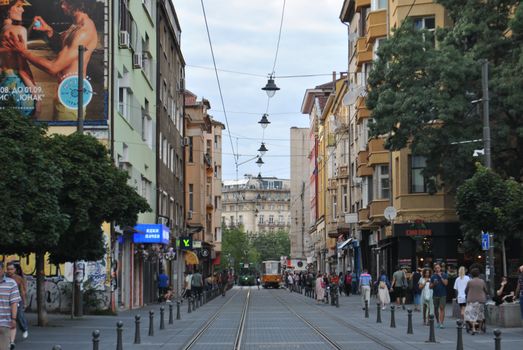 Vibrant city street scene with tram, pedestrians, and colorful architecture during the day.