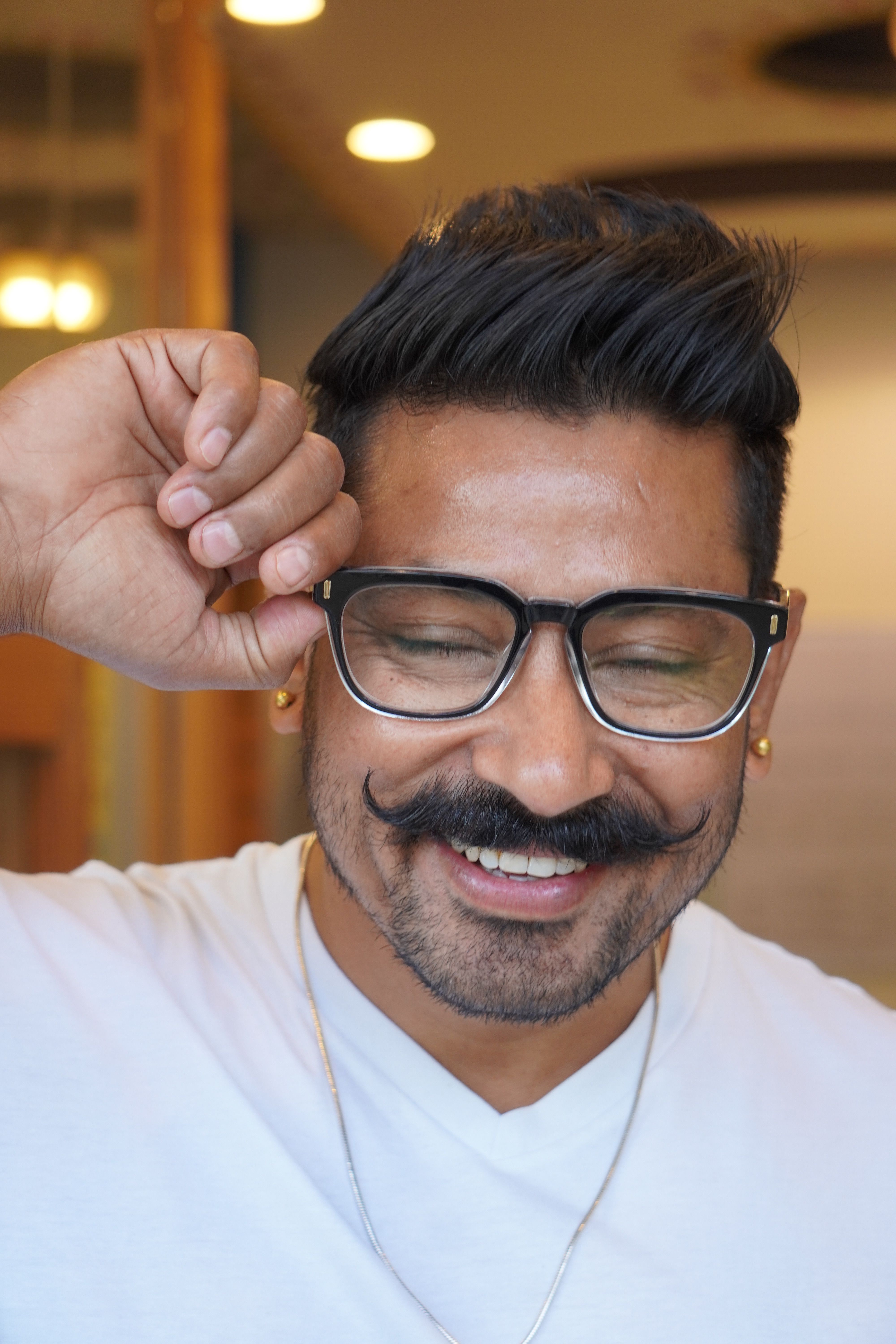 Portrait of a joyful man with glasses and a vintage mustache, smiling indoors.