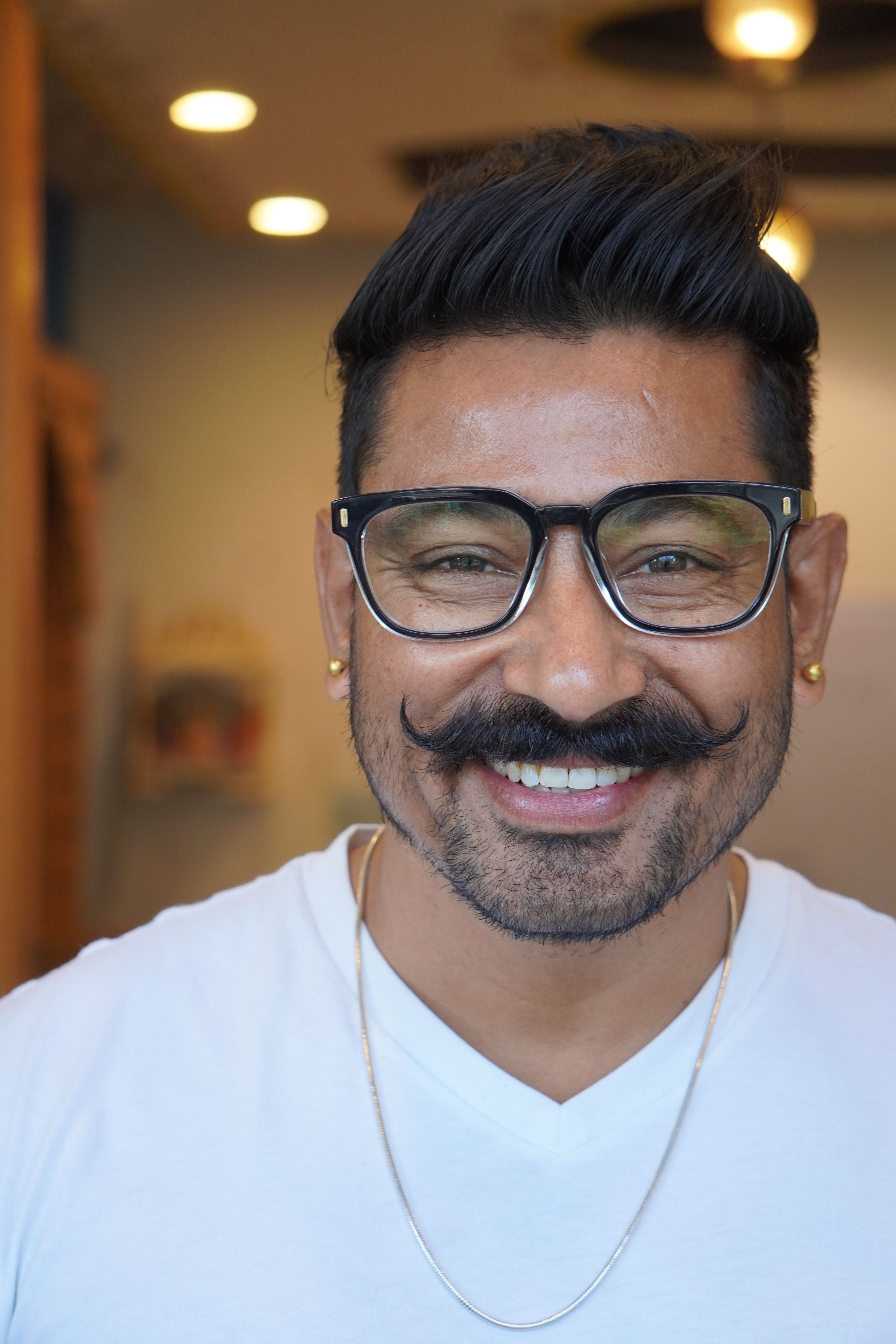 Close-up portrait of a smiling man with glasses and a distinctive curled mustache.