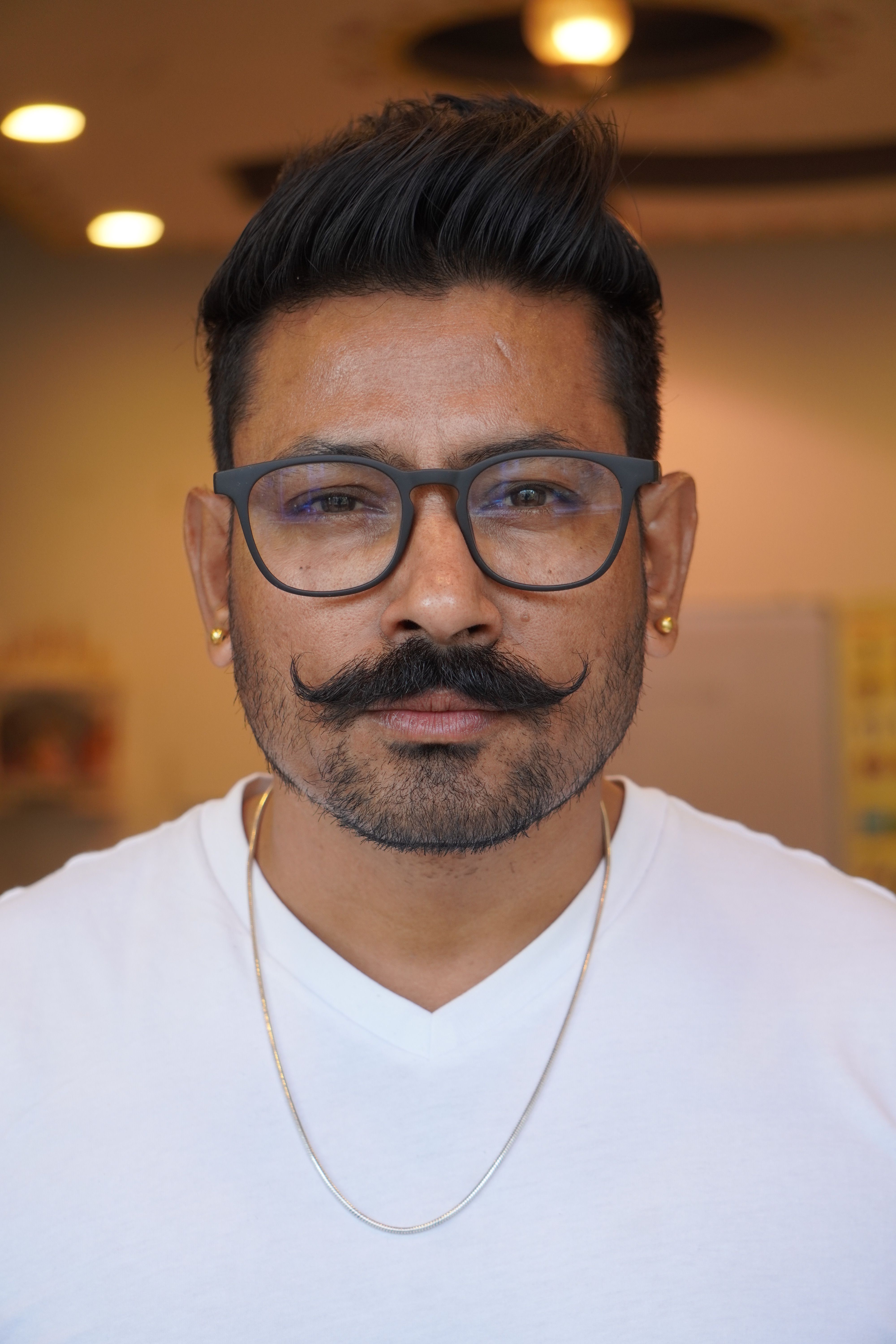Close-up portrait of an adult man with eyeglasses, mustache, and white shirt.