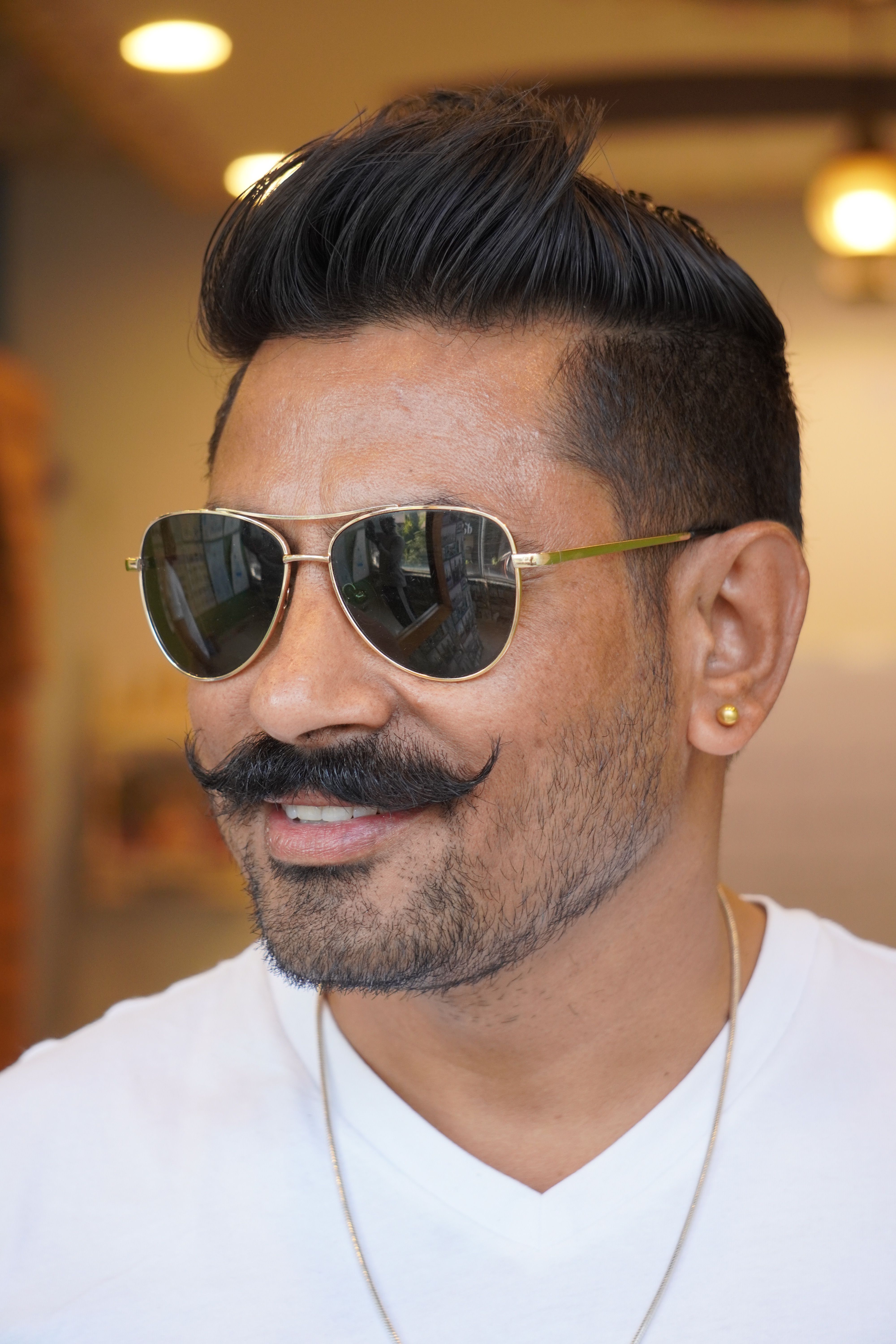 Portrait of a stylish man with sunglasses, mustache, and confident smile indoors.