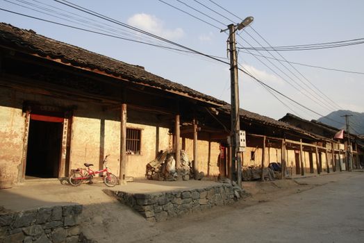 Sunlit traditional street with rustic architecture and a parked red bicycle in an Asian village.