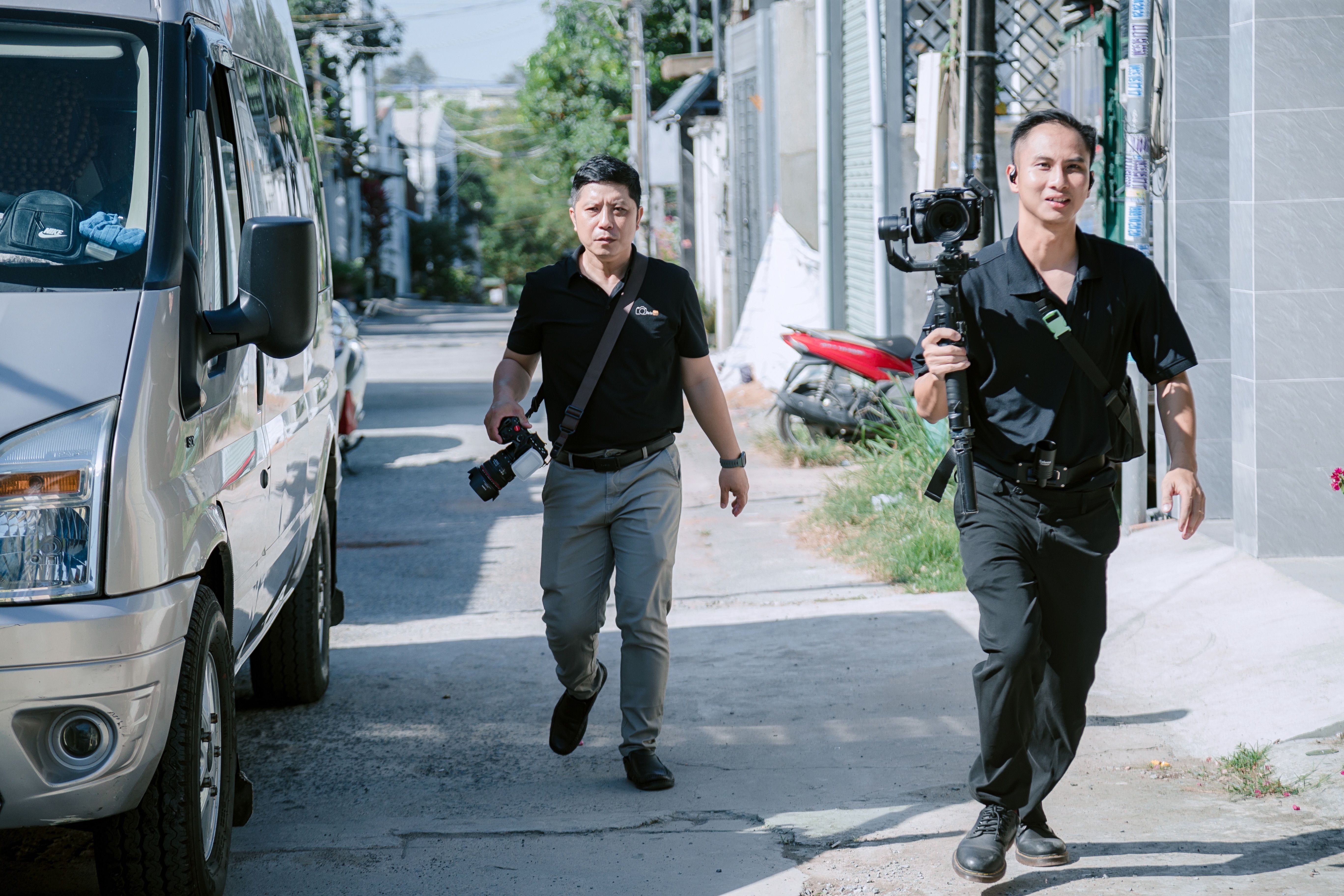 Two photographers with equipment walking in a sunny urban street, capturing moments.