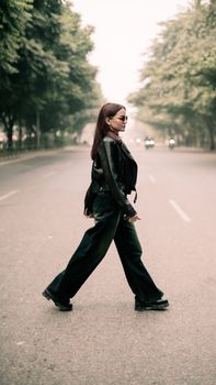 Confident woman in leather jacket and pants crossing an empty street during daytime.