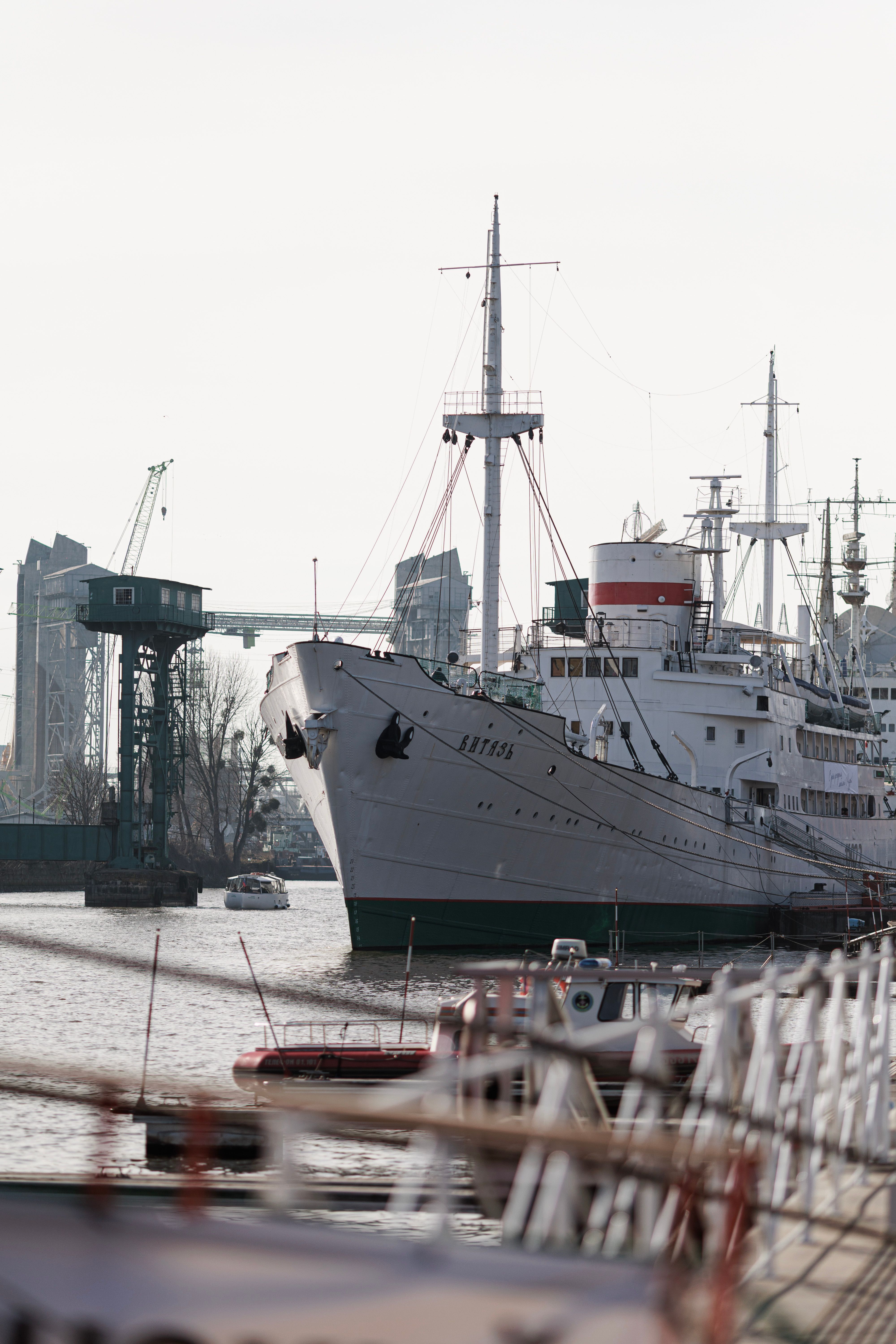 A large ship docked in an urban harbor, surrounded by cranes and smaller boats.