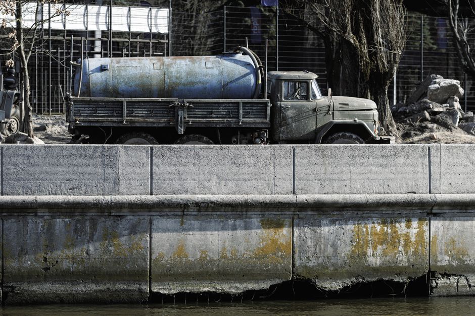 A vintage cement mixer truck parked by a canal with visible signs of wear and weathering.