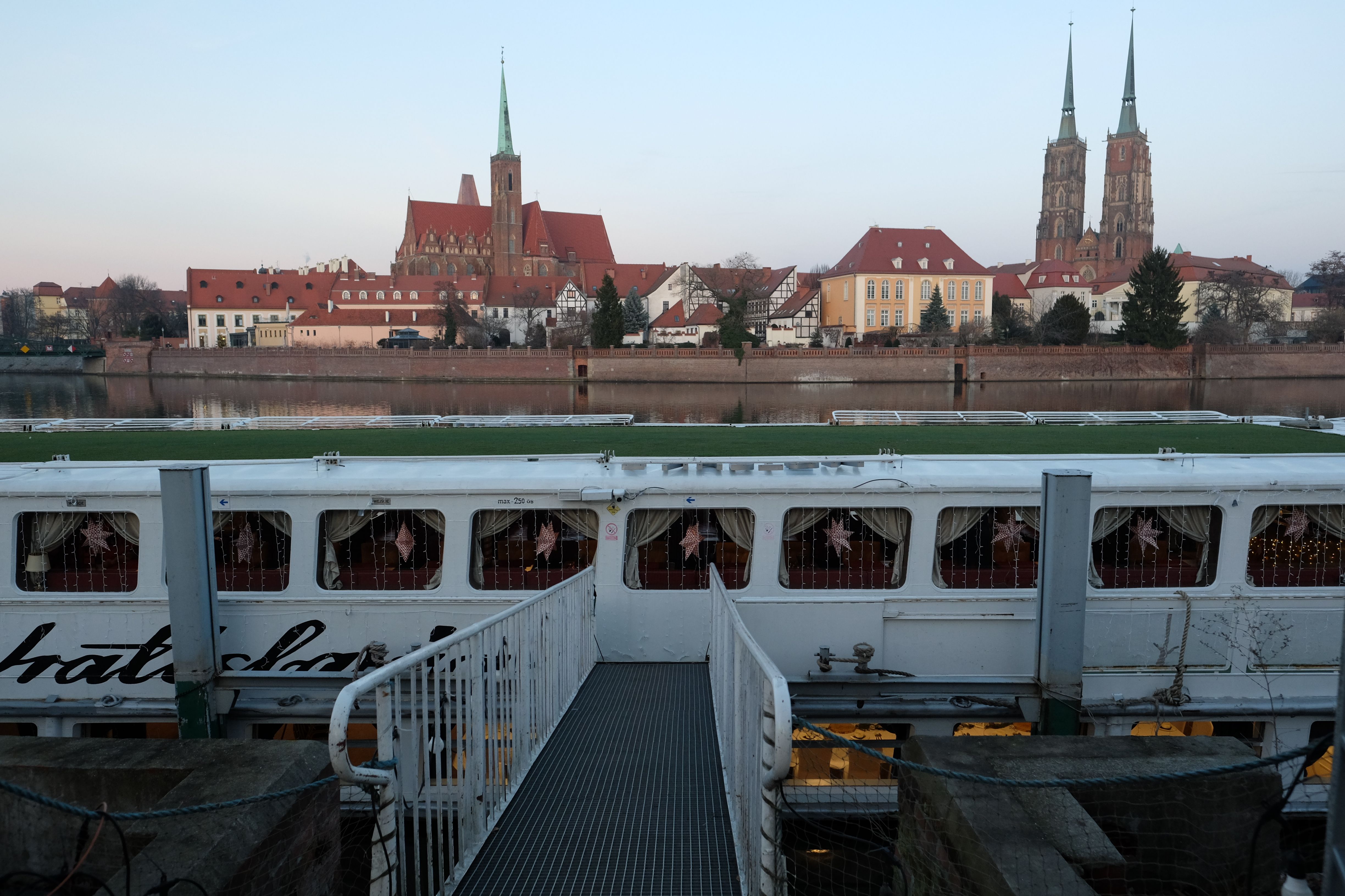 View of Wrocław Cathedral and the river with a docked boat at twilight, showcasing historic architecture.