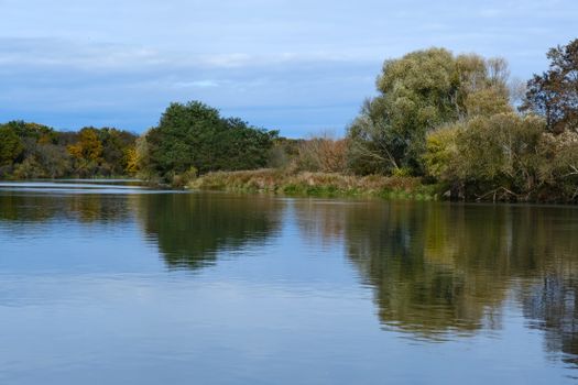 Serene river scene with reflections and fall foliage, blue sky overhead.