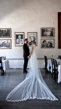A bride and groom holding hands in a decorated indoor venue with elegant portraits on the wall.