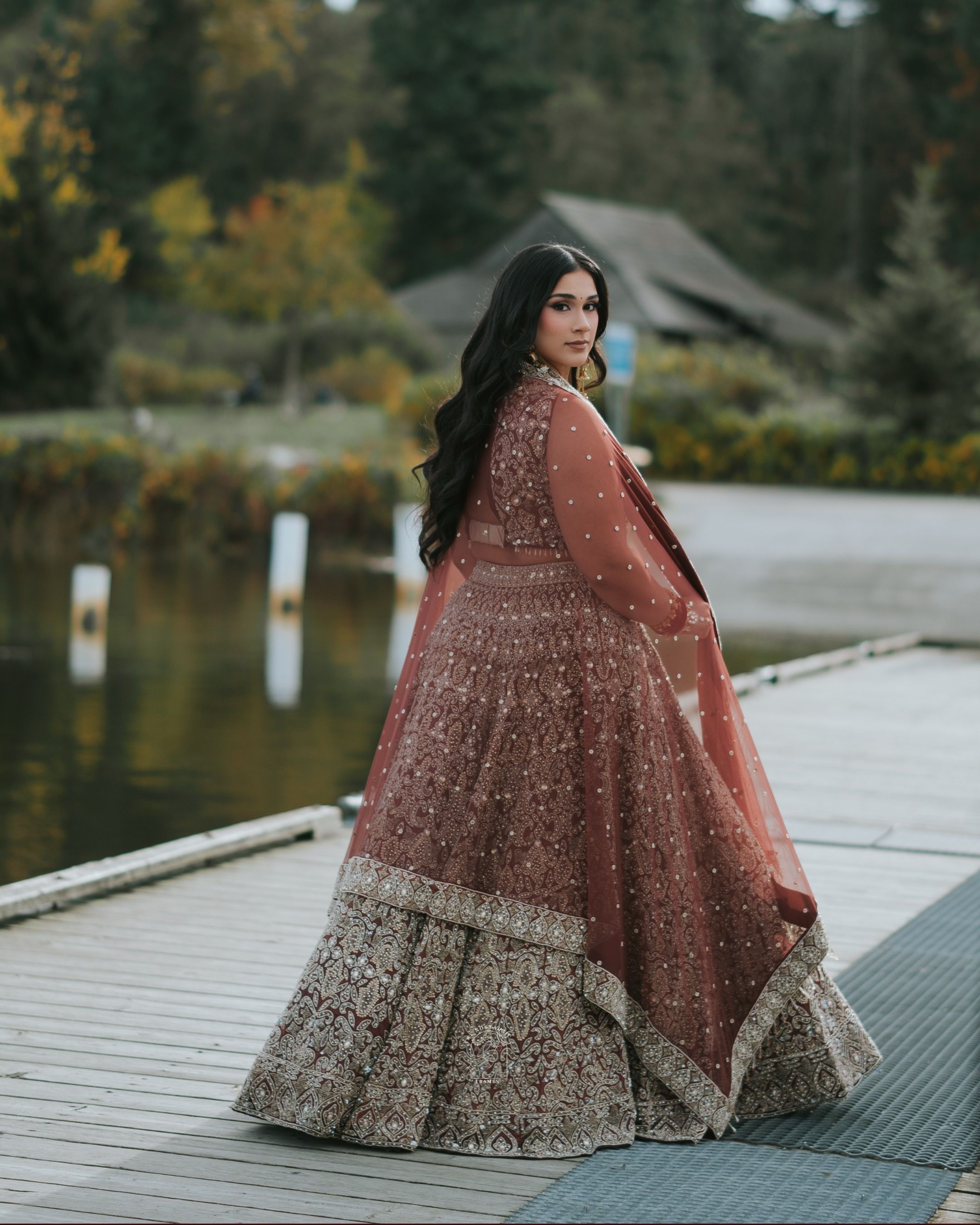 Woman in a beautiful traditional dress stands by a serene lakeside, reflecting elegance.