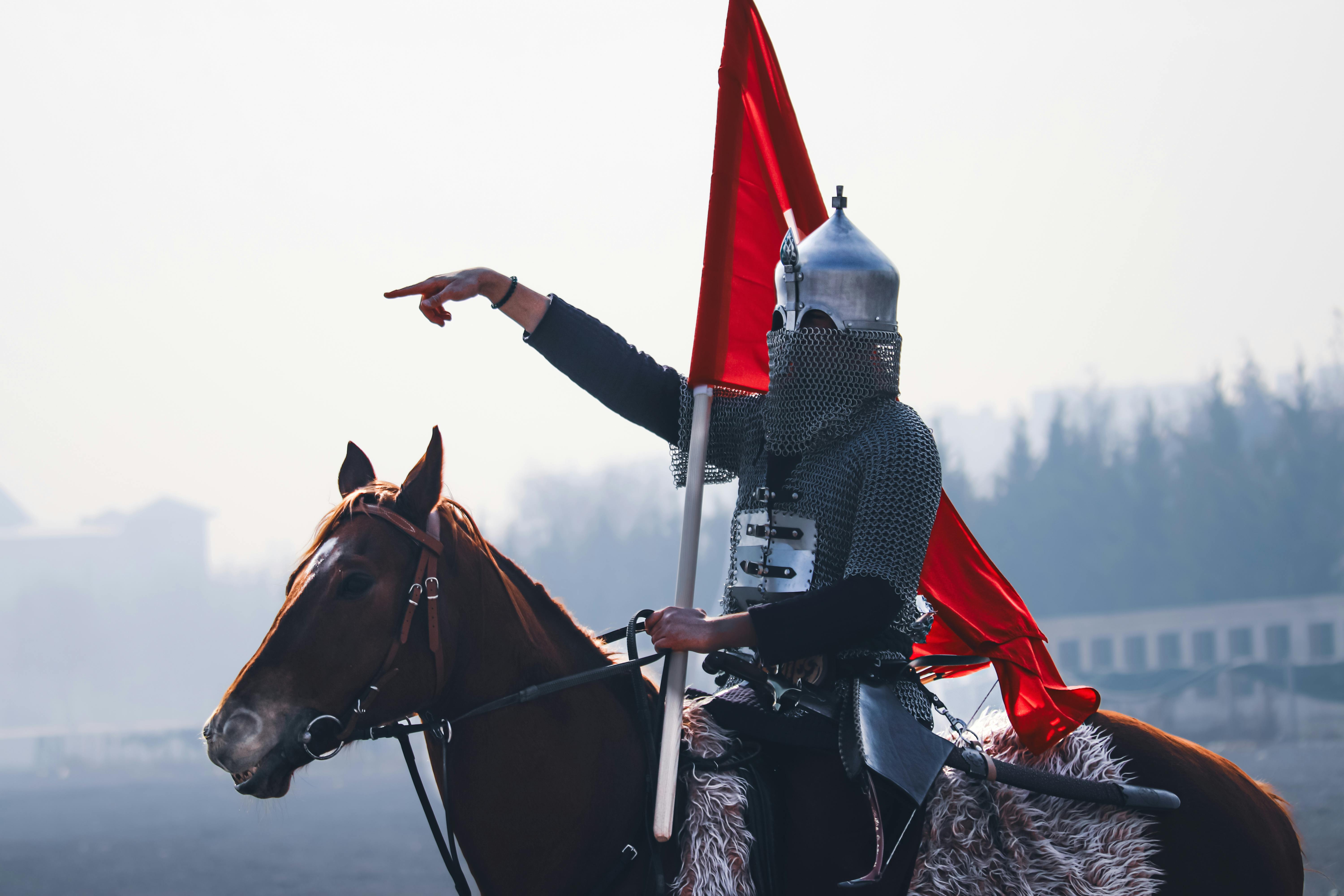 A medieval warrior in armor riding a horse holding a flag, outdoors in Konya, Türkiye.