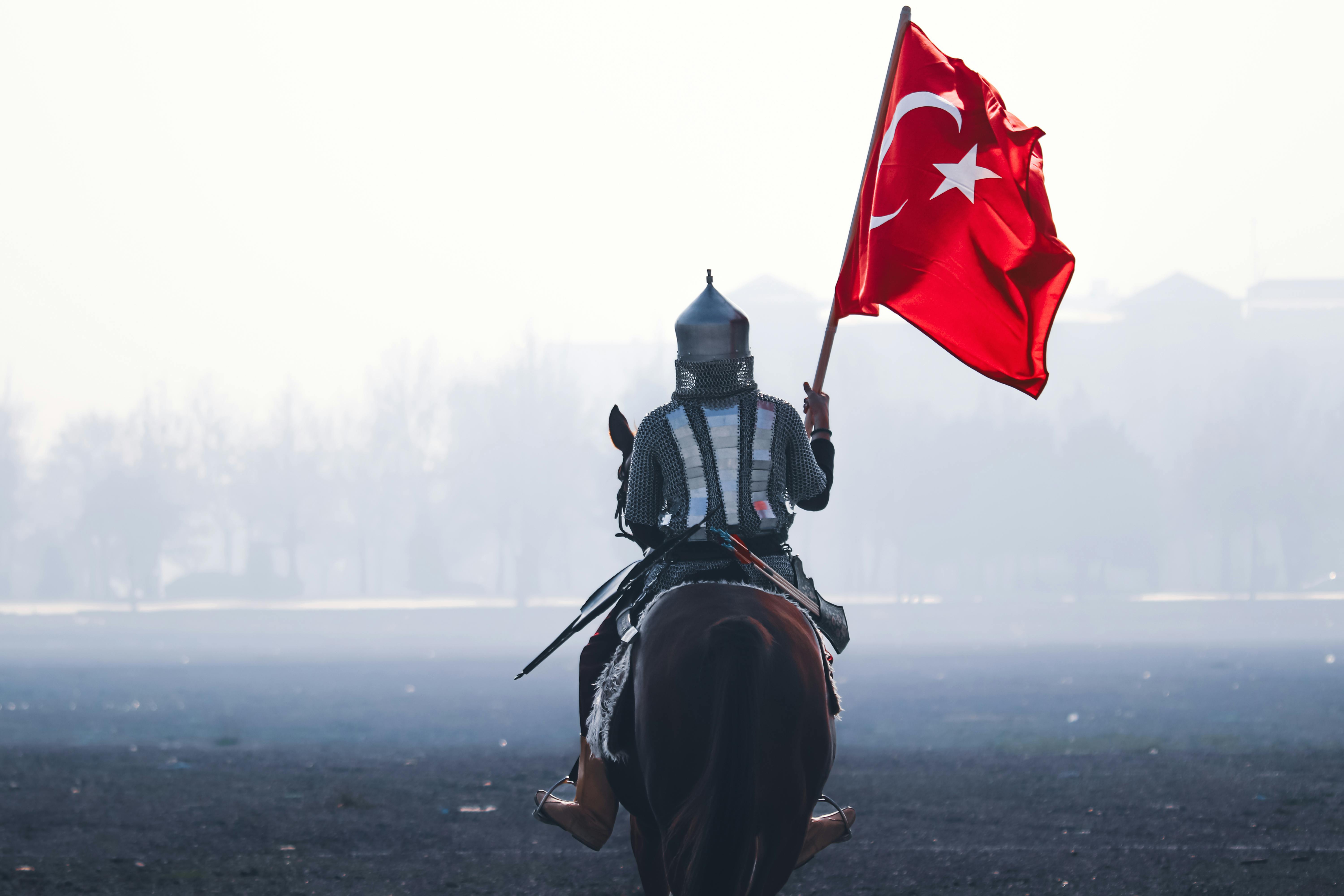 A historical reenactor in armor riding horseback carries the Turkish flag in Konya, Türkiye.
